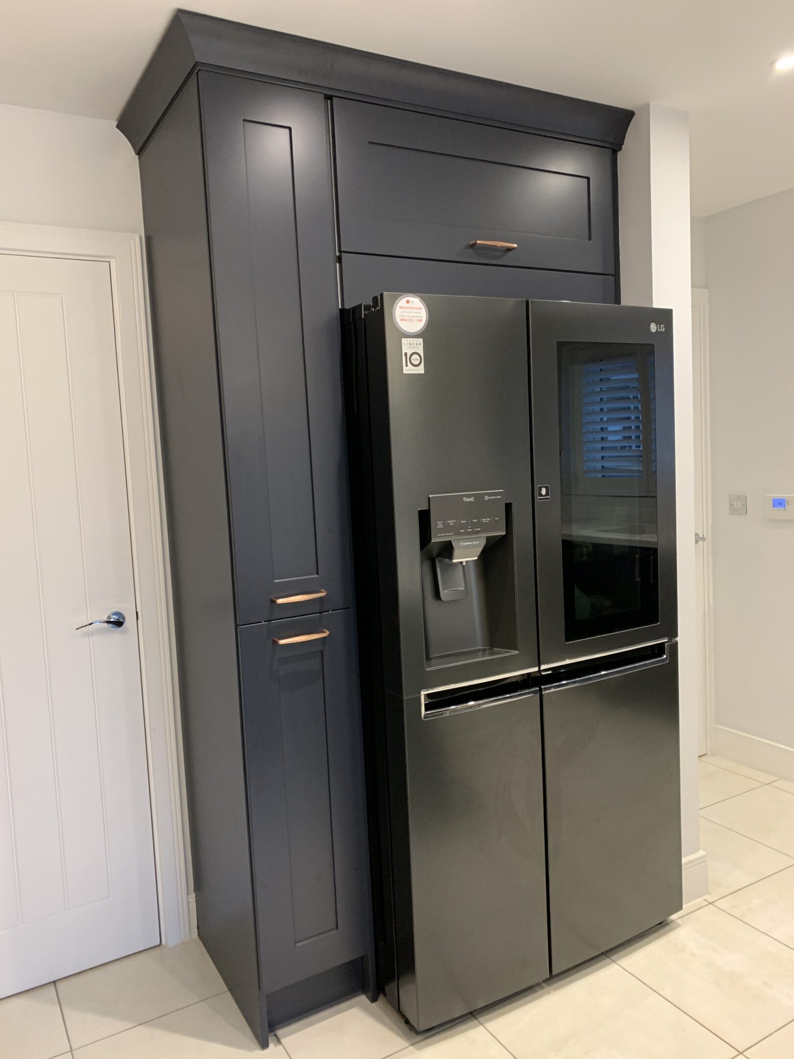 Black stainless French-door refrigerator beside navy cabinets