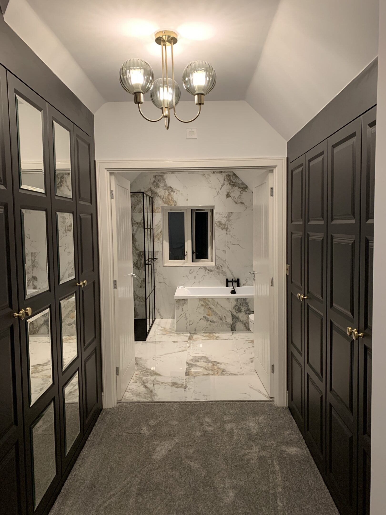 Closet-lined hallway leading to marble bathroom